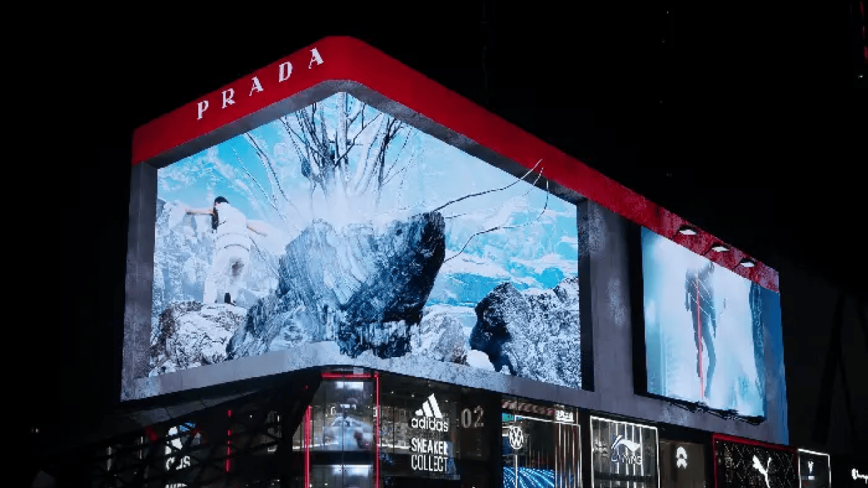 Close-up of a 3D Prada Linea Rossa billboard featuring a dynamic mountain scene, displayed at night.